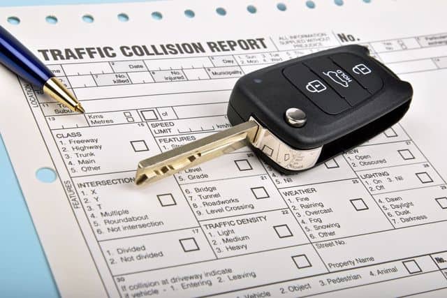 A copy of a car accident police report with a car key resting on top of it. 
