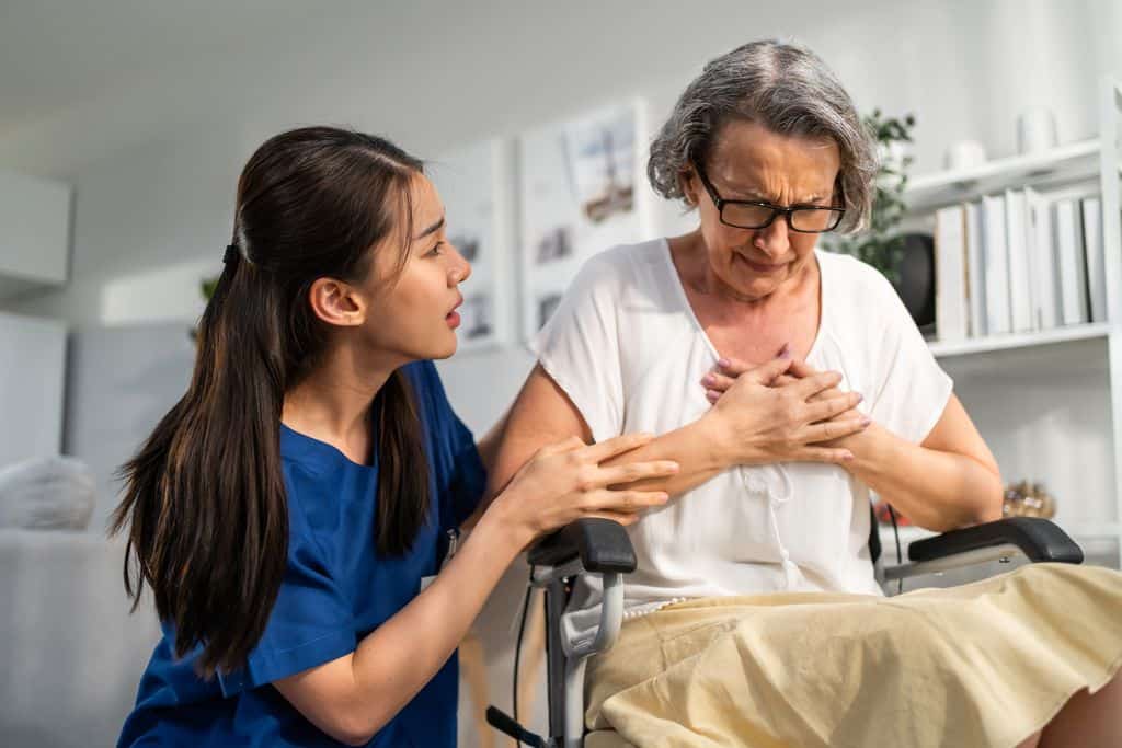 An older woman in a wheelchair clutches her chest in pain after sustaining bruises across her body from her seat belt in a car wreck. A nurse tries to comfort her.