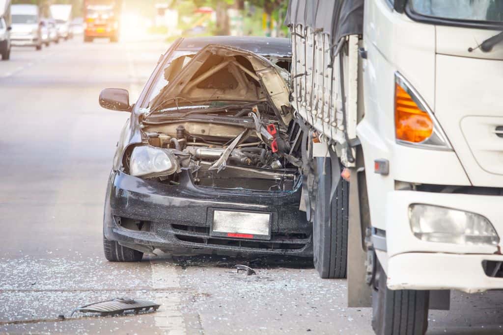 the damaged front end of a car after it collided into the back end of a large truck.