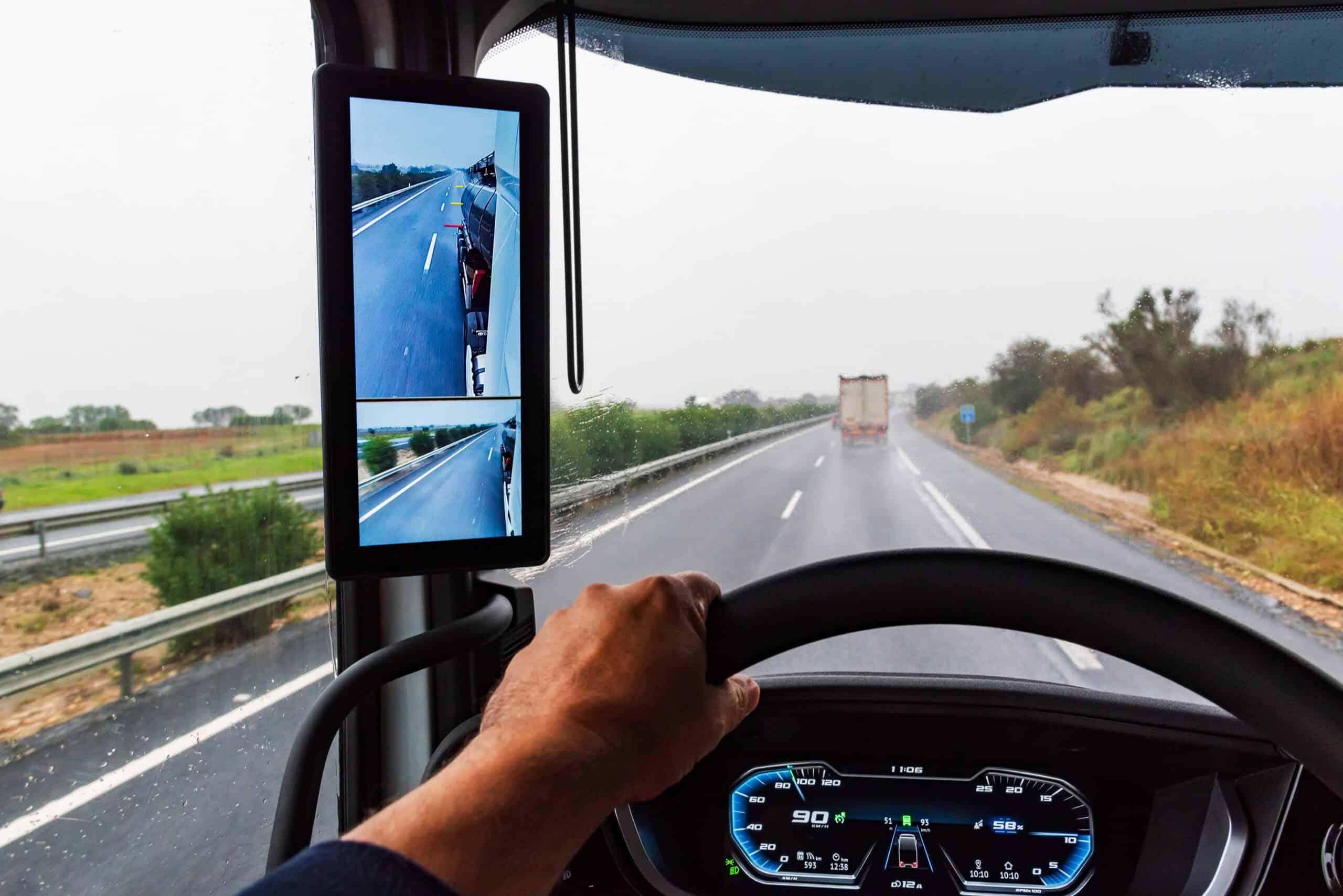 A commercial truck traveling down the highway with a view of their rear-view mirror.