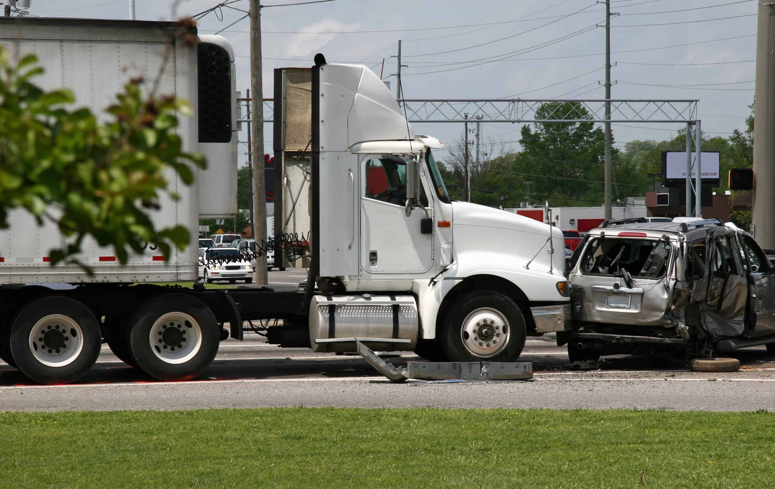 A semi-truck crashes into a grey passenger mini-van, causing severe damage to the van.